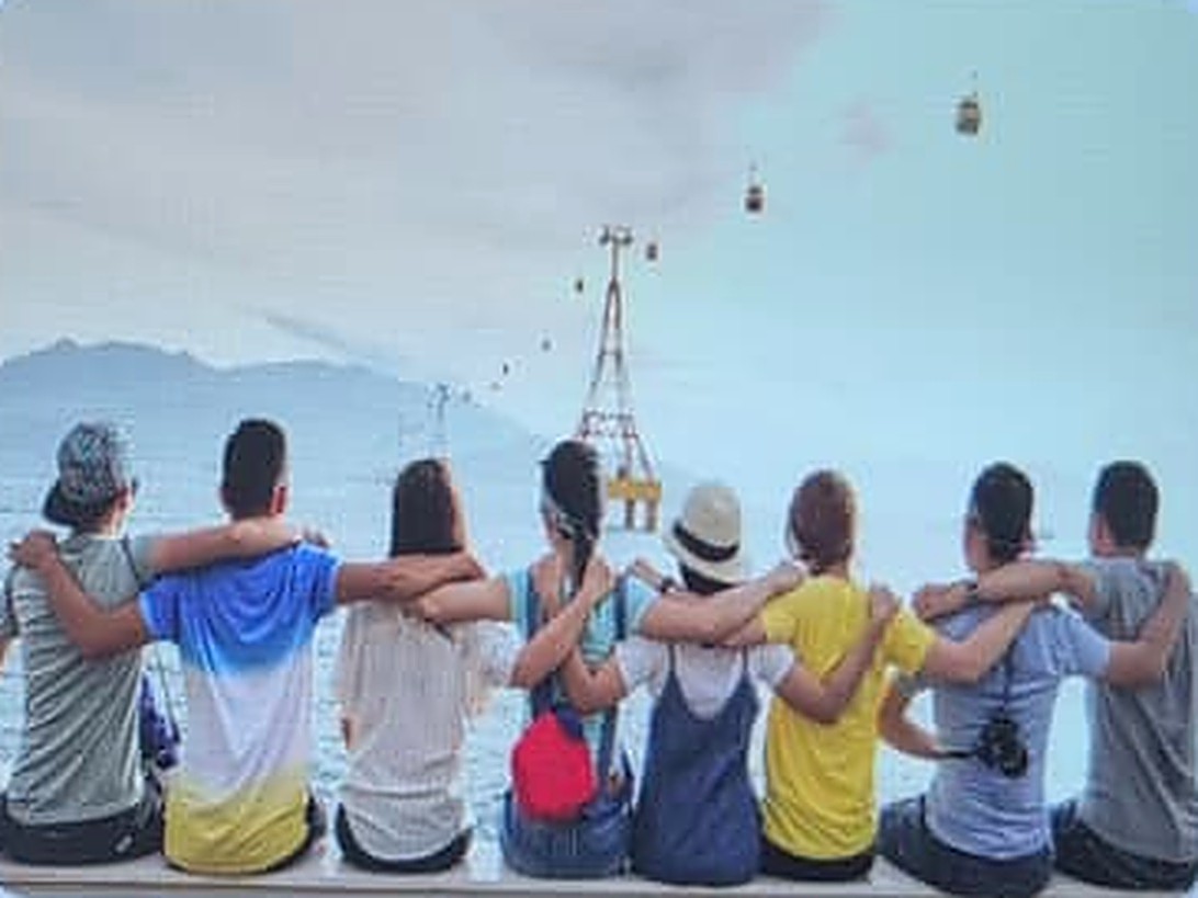 Young people sitting arm in arm, looking out over the water